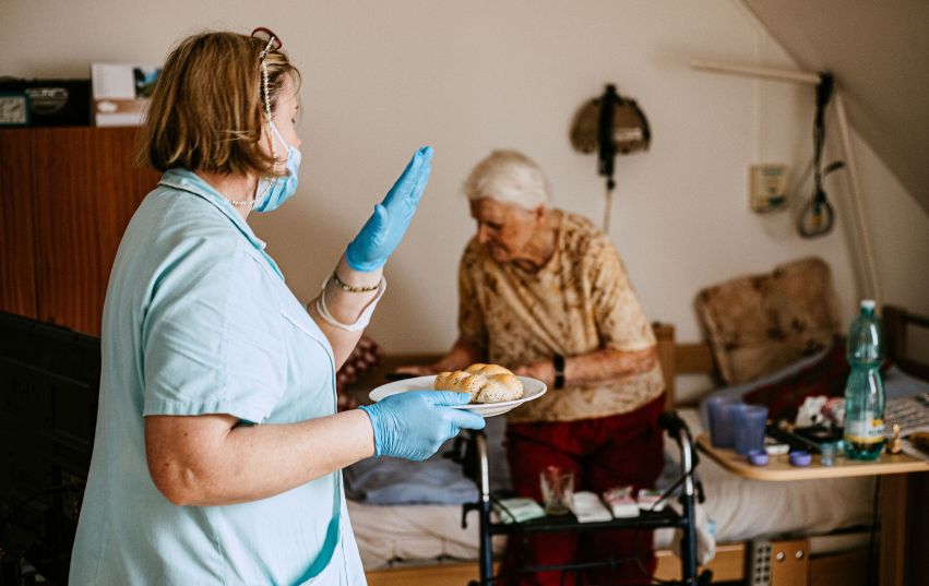 Pečovatelka nese svačinu seniorce v domově seniorů